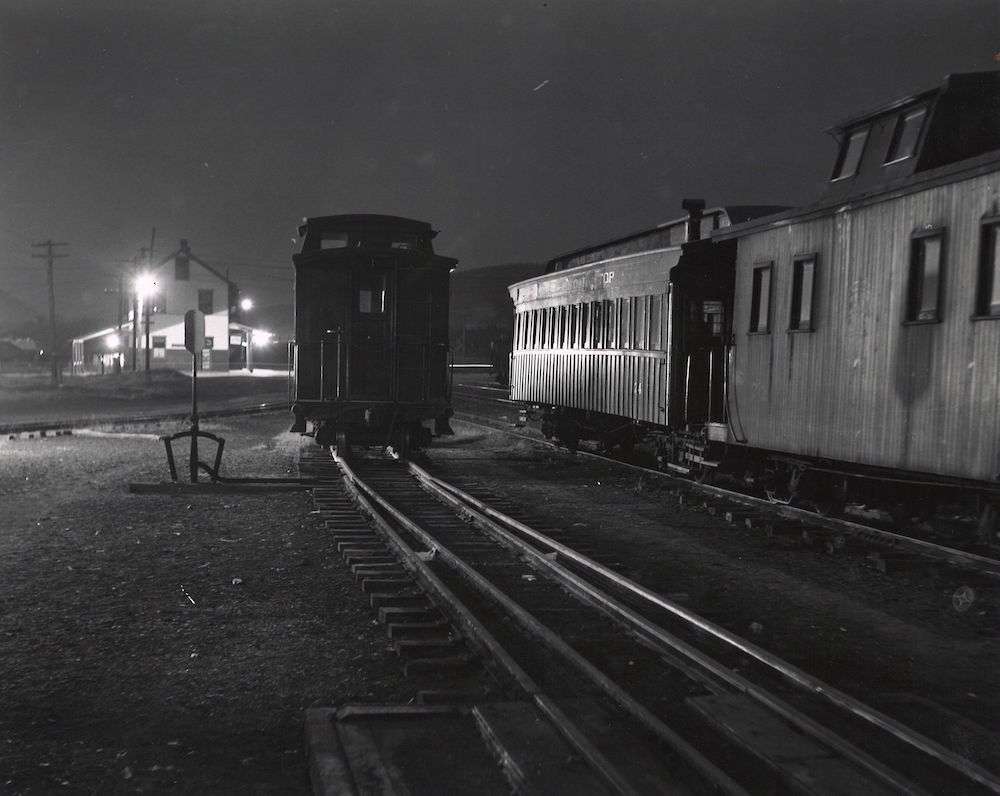 Cabooses and passenger cars at a railyard during the evening.