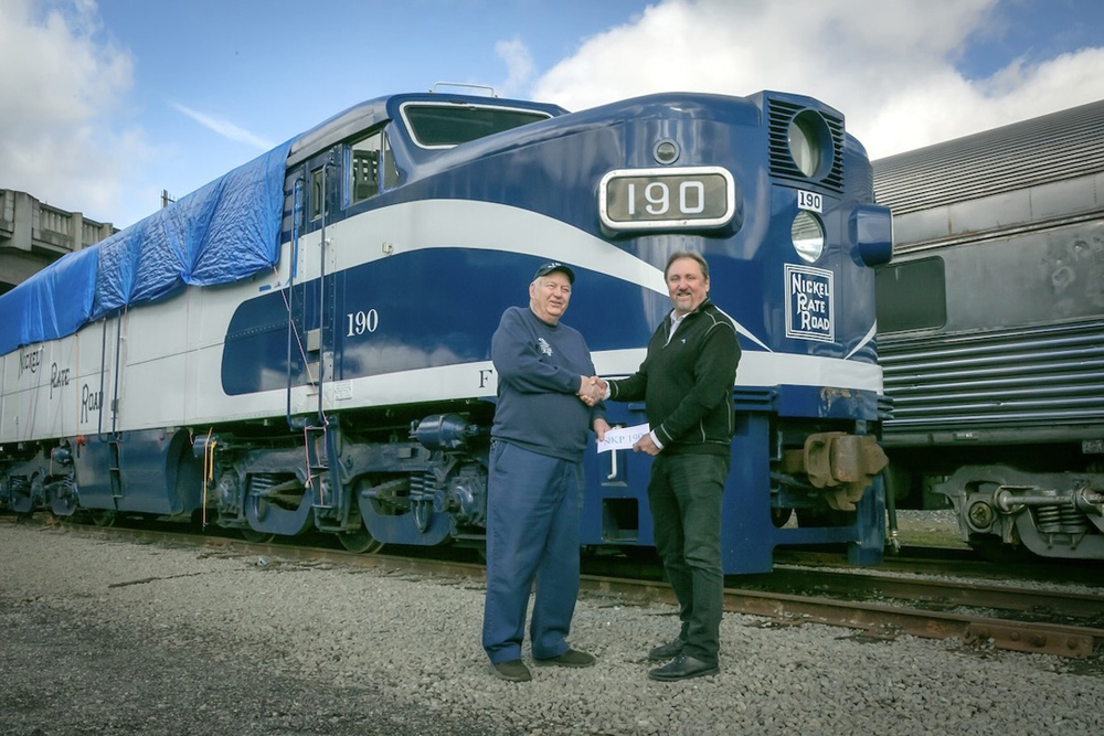 Men shaking hands in front of blue and white diesel locomotive