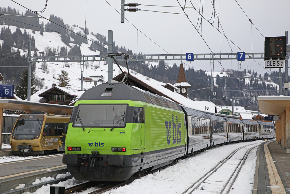 Bright green locomotive on passenger train in snow-covered mountain town