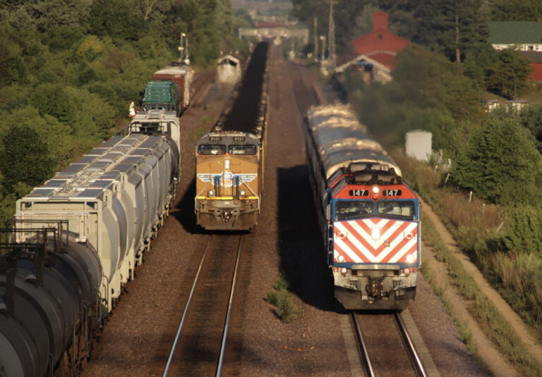 Commuter train and two freight trains in setting sun.
