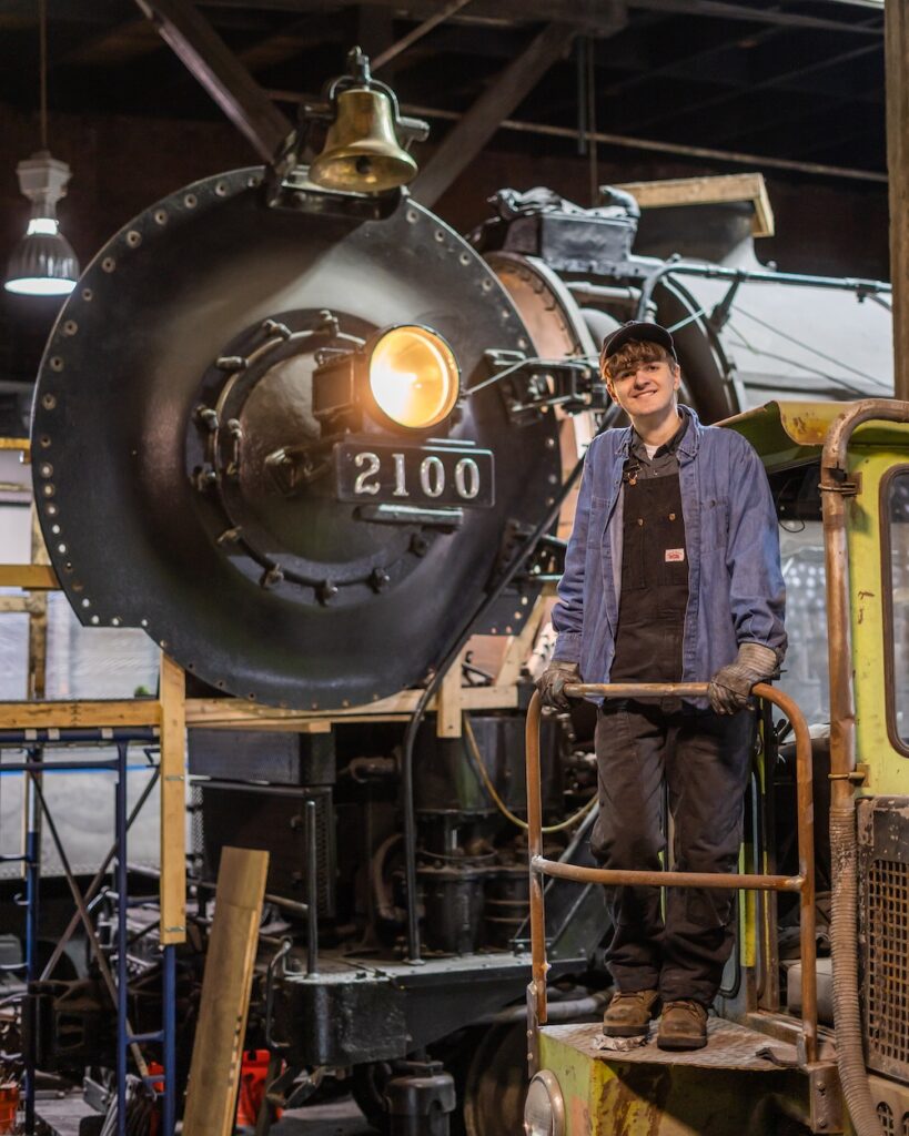 Young volunteer standing in front of steam locomotive being restored.