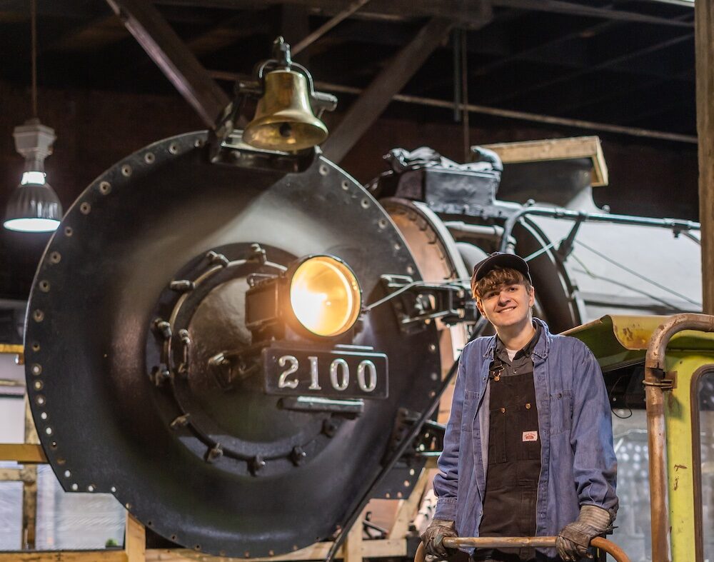 Young volunteer standing in front of steam locomotive being restored.