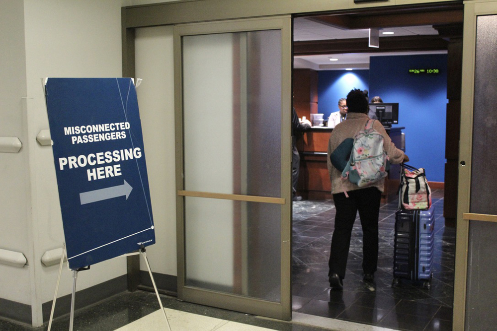 Person standing in doorway next to sign reading "Misconnected passengers, enter here."