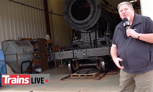 Man standing in front of a steam locomotive that is being worked on.