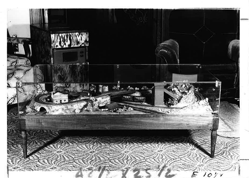black and white image of small train layout built into a glass-topped living room table
