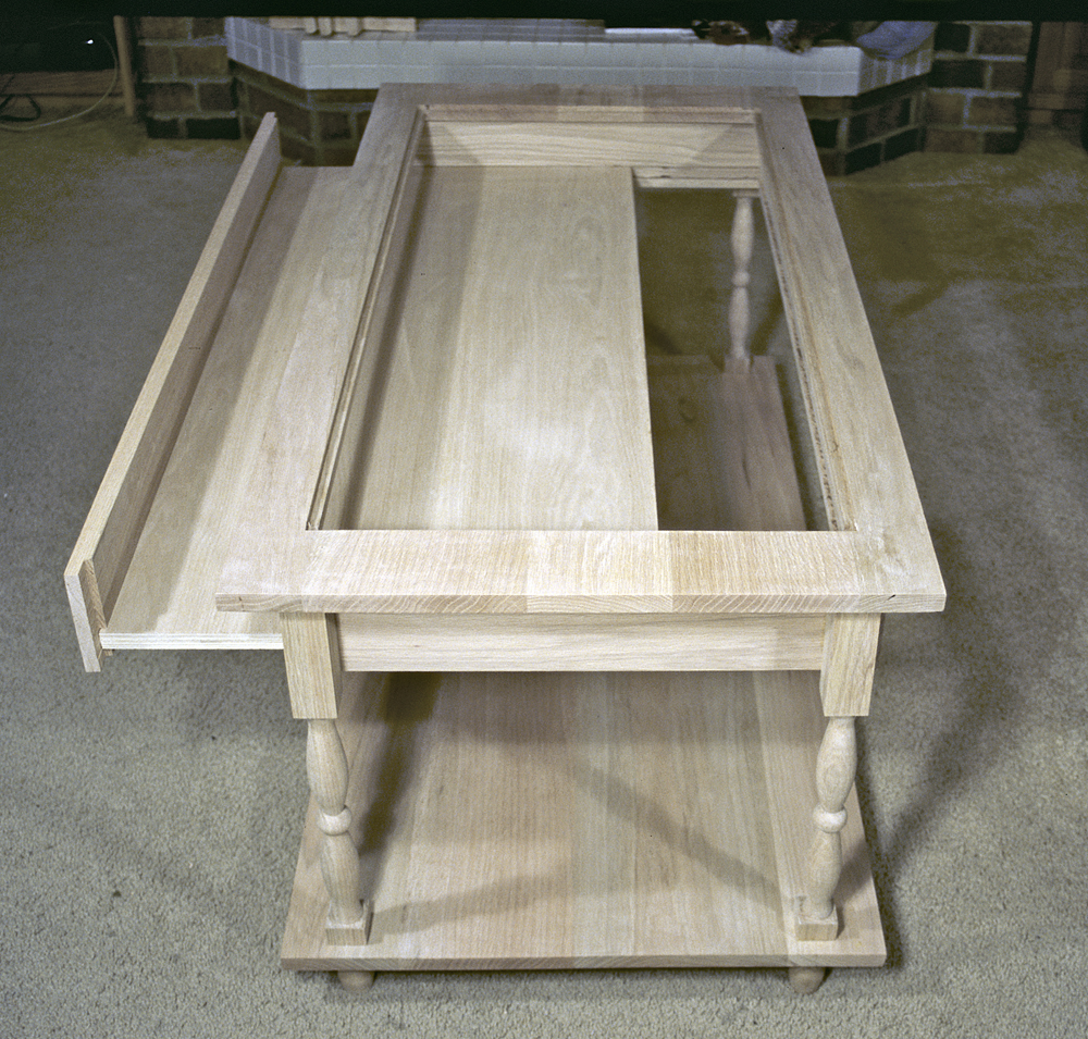 bare wood coffee table with larger side drawer open in top sitting on tan carpet