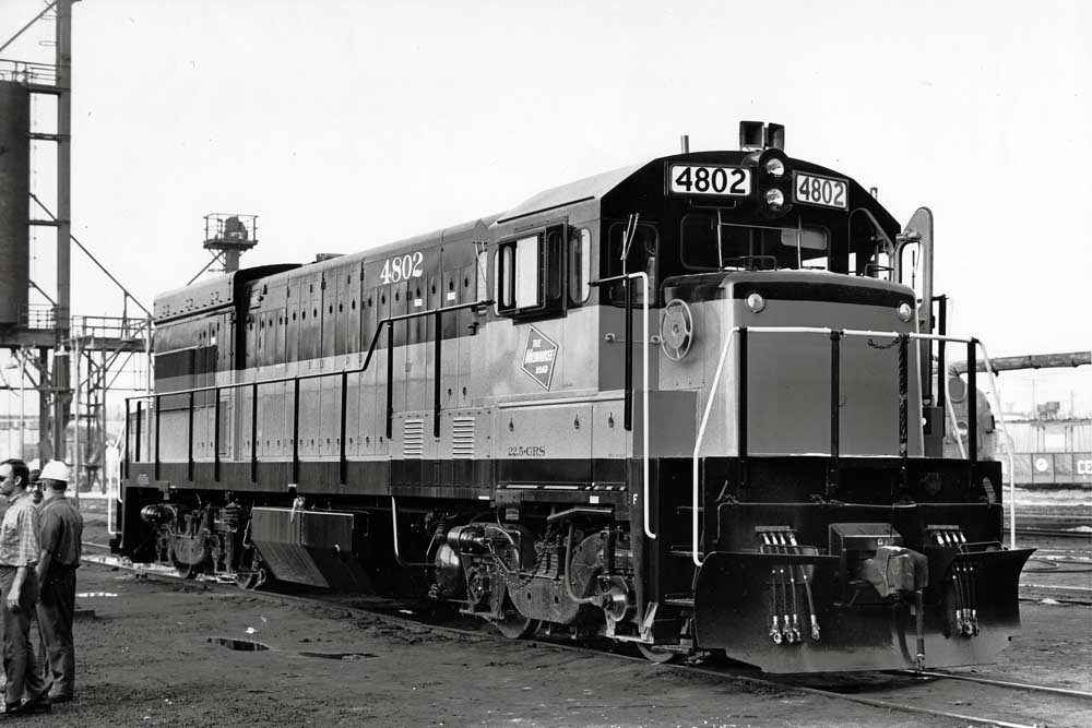 Two-tone diesel locomotive with people in rail yard