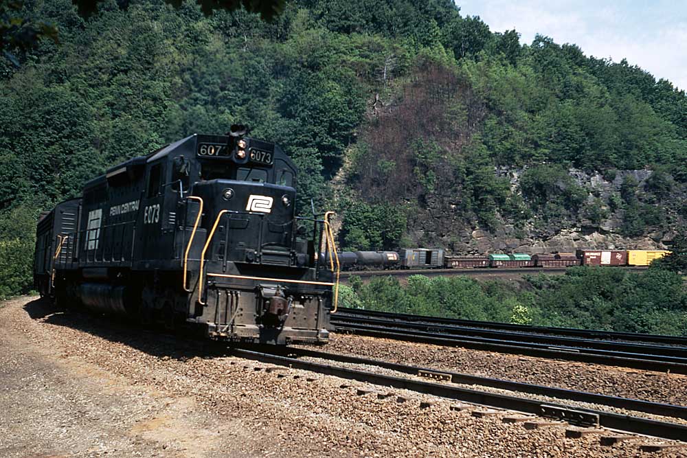 Black-and-white locomotives on Penn Central history freight train curving through mountains