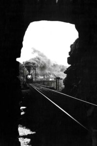 Steam locomotive with train on bridge approaching tunnel