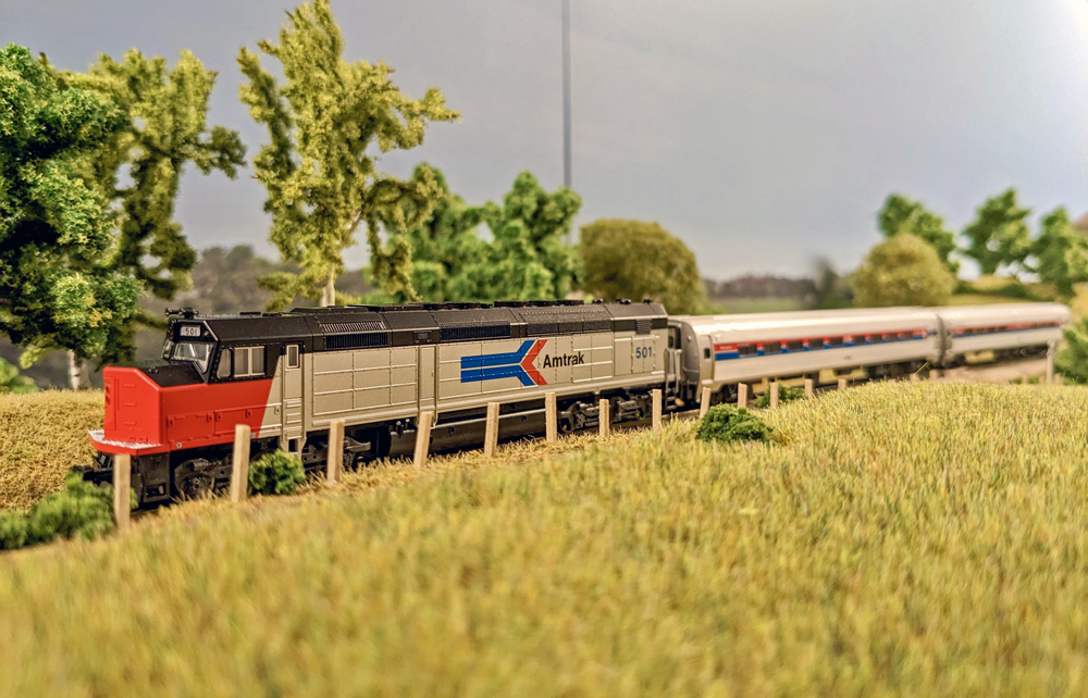 A model passenger train travels past a field