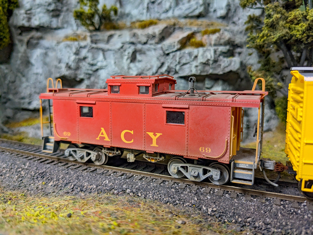 Model of a red caboose follows a yellow boxcar