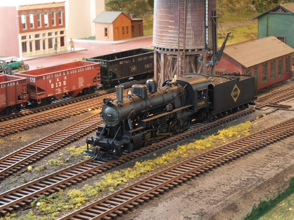 A model steam locomotive sits under a water tower.