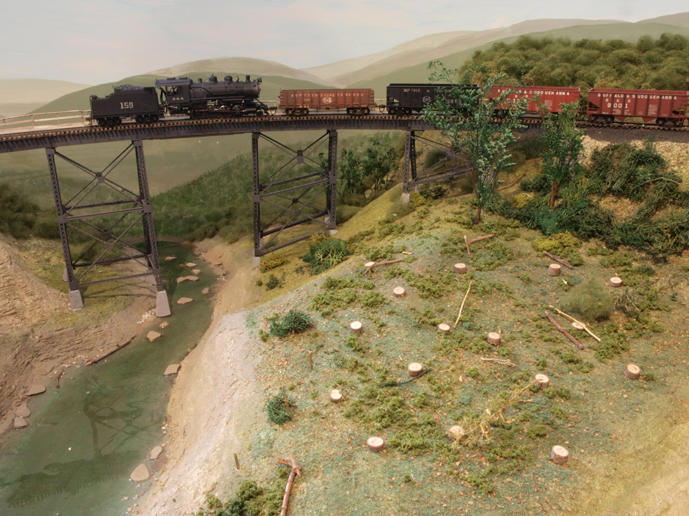 A model steam engine pushes hoppers over a bridge.