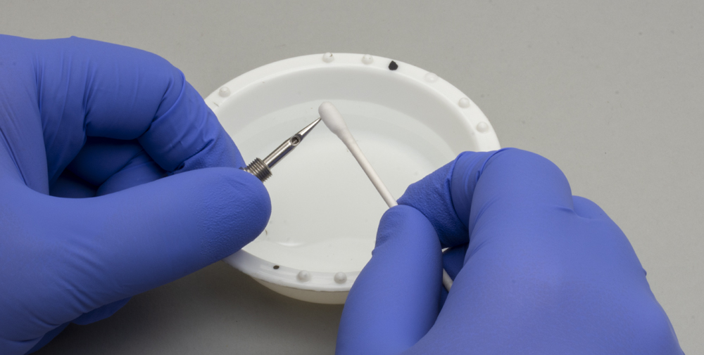 Color photo of airbrush tip being cleaned with cotton swab.