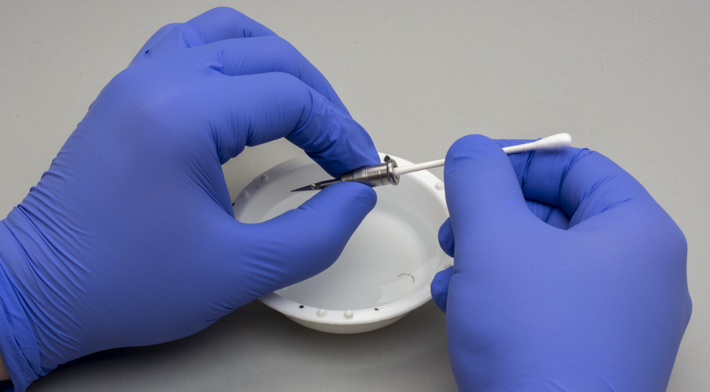 Color photo of cotton swab being used to clean airbrush part.