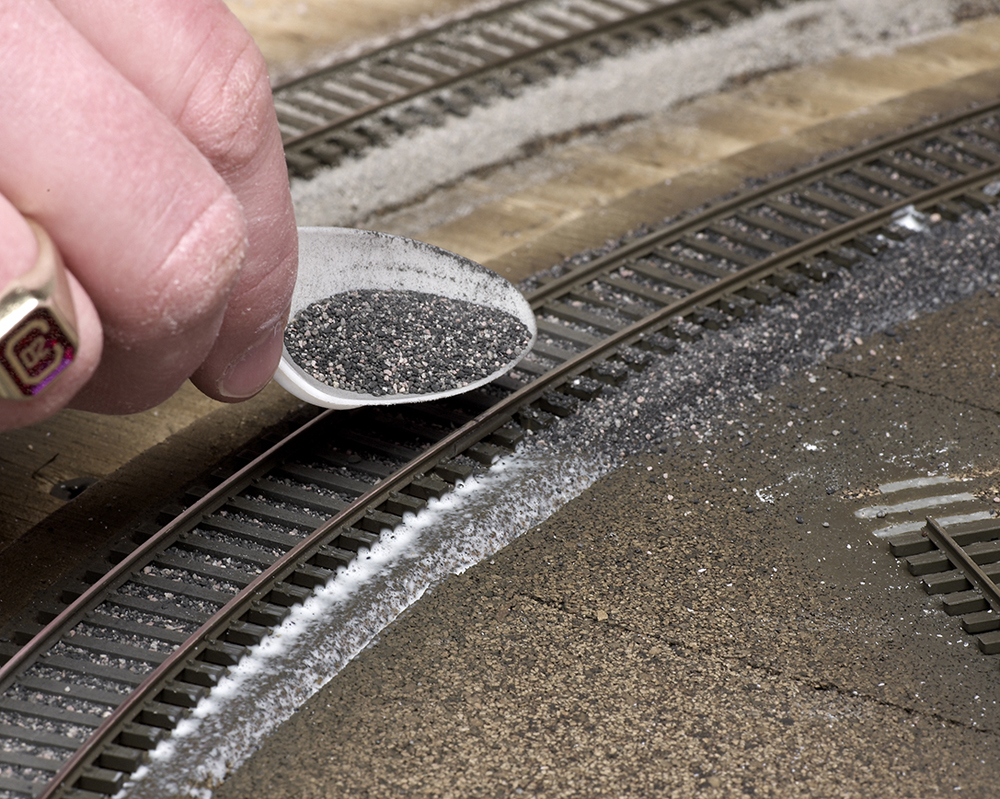 Color photo of ballast being sprinkled into glue with a spoon.