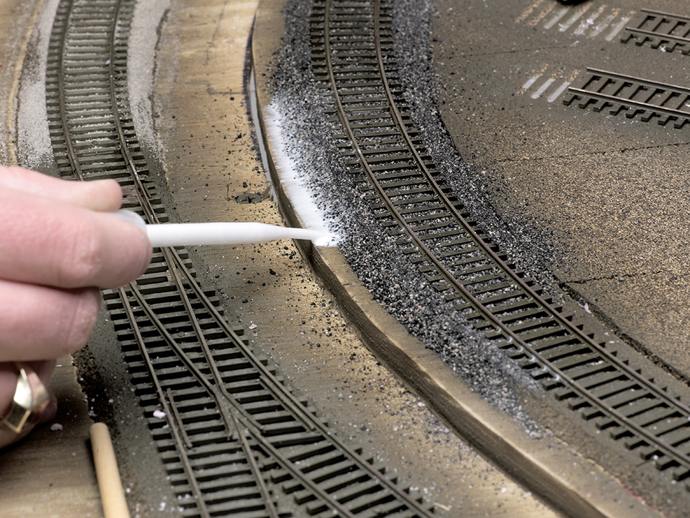 Color photo of scenery glue being applied to ballast with a pipette.