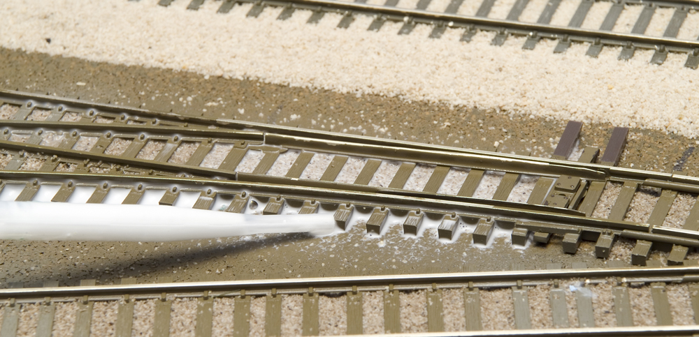 Color photo of scenery glue being applied to ballasted turnout.