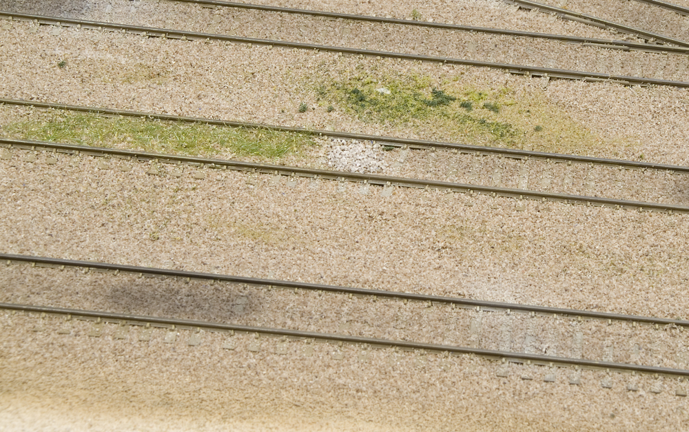 Color photo of ballasted yard tracks with additional weathering and scenery.