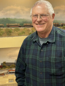 Man in plaid shirt stands near HO scale layout