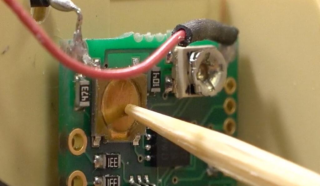 A closeup of a model train decoder with a button being pressed with a small wooden rod