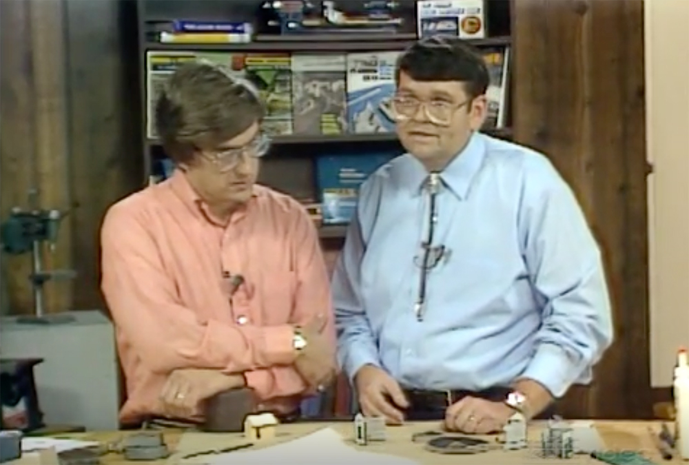 An image of two men standing behind a modeling workbench