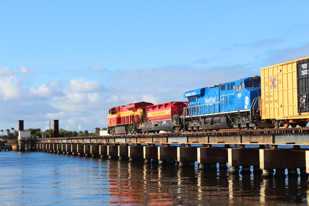 Diesel train locomotives crossing river bridge.