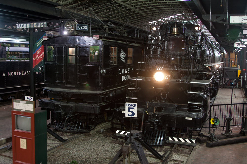 Electric boxcab locomotive and a Yellowstone steam locomotive in a museum exhibit hall.