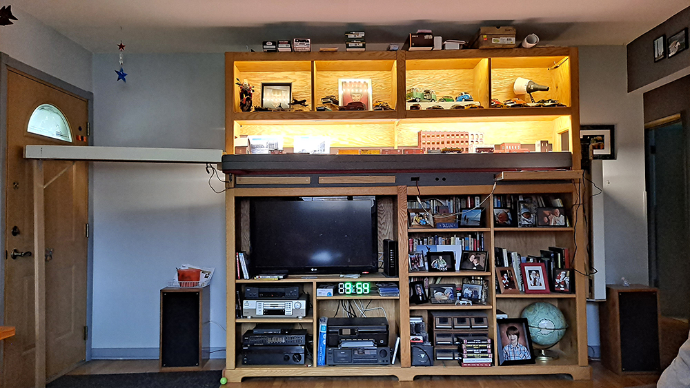 Brown bookcase with assorted books and a gray TV on it, plus one shelf contains small model trains