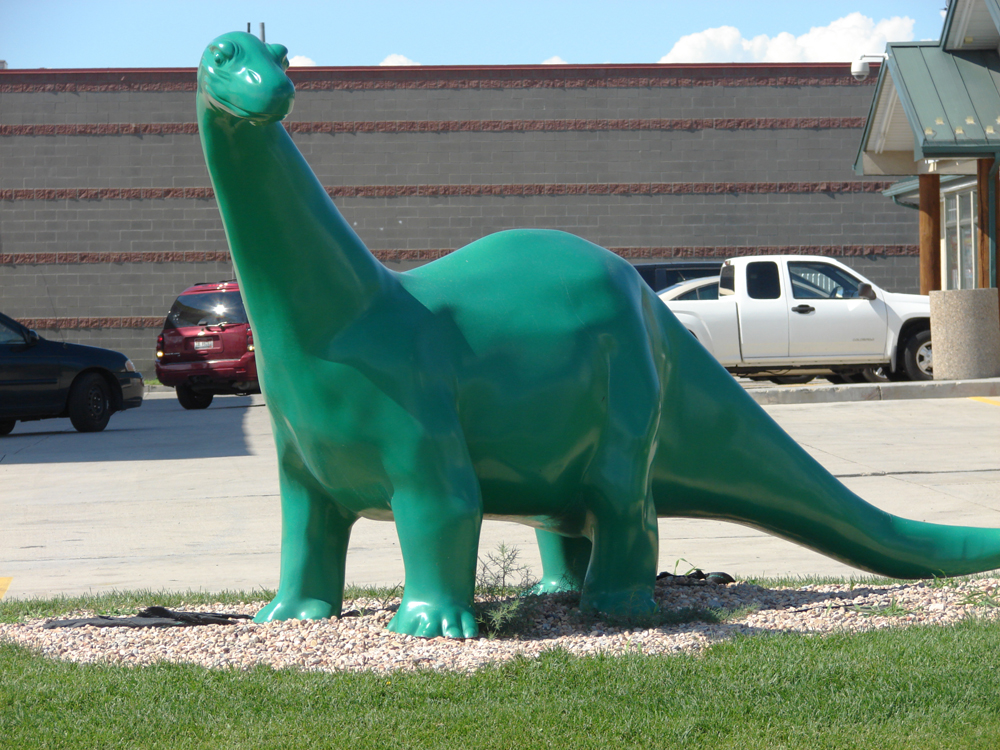 green dinosaur statue in front of a gas station