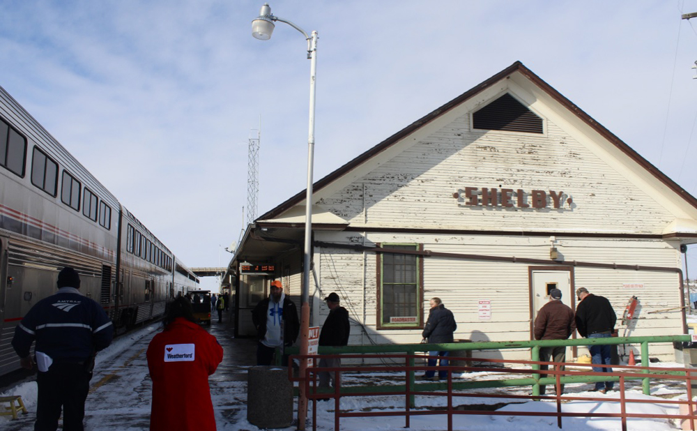 Passenger train stopped at wood-sided station building.