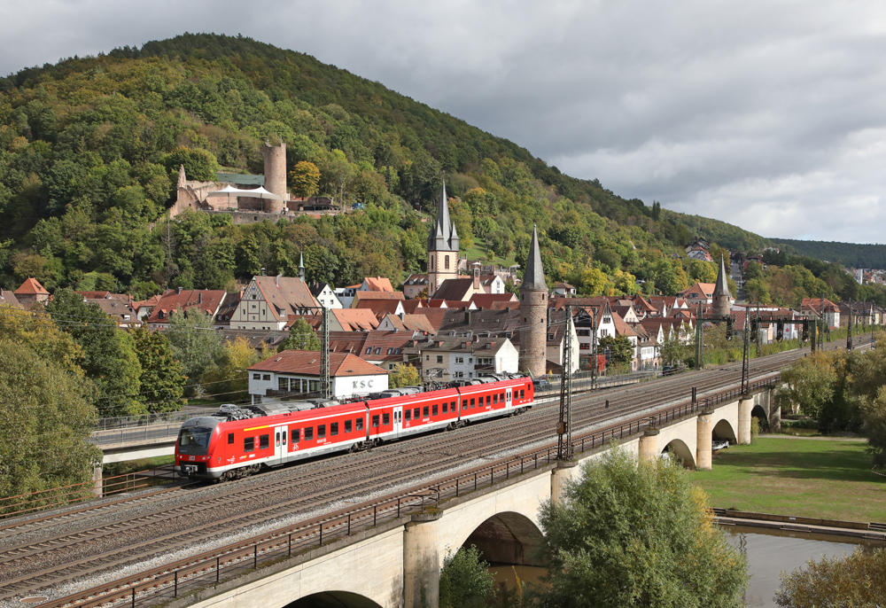 Three-car red passenger train on bridge crossing river