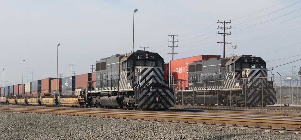 Two black and silver locomotives with strings of containers