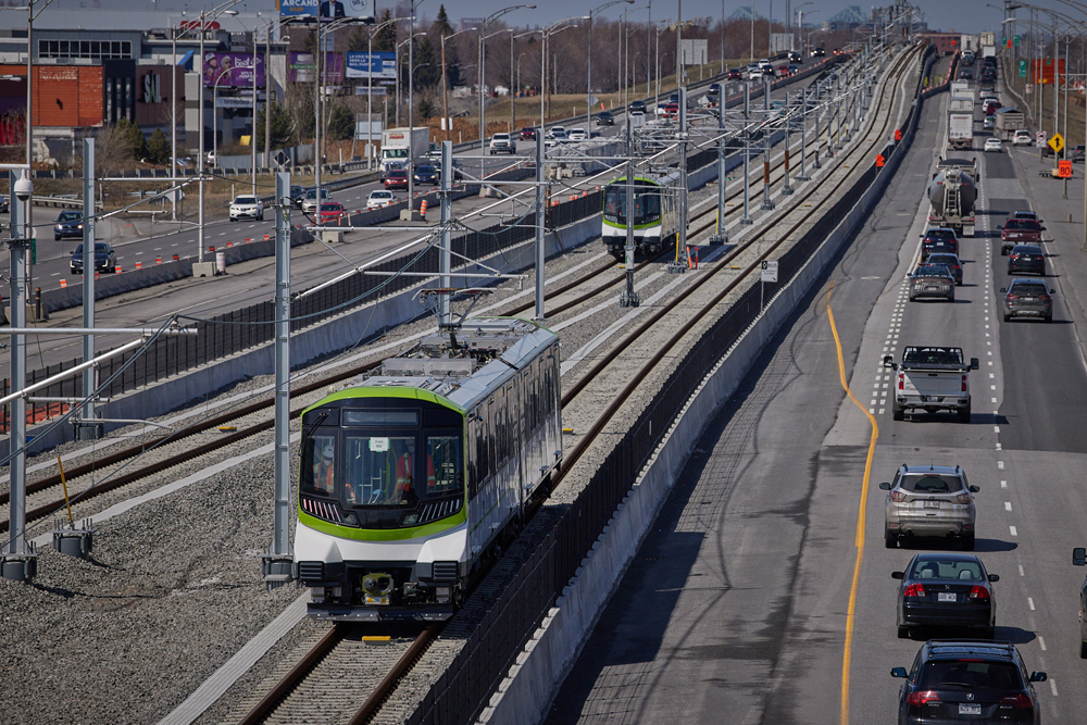Two light rail trains running on track in center divider of highway