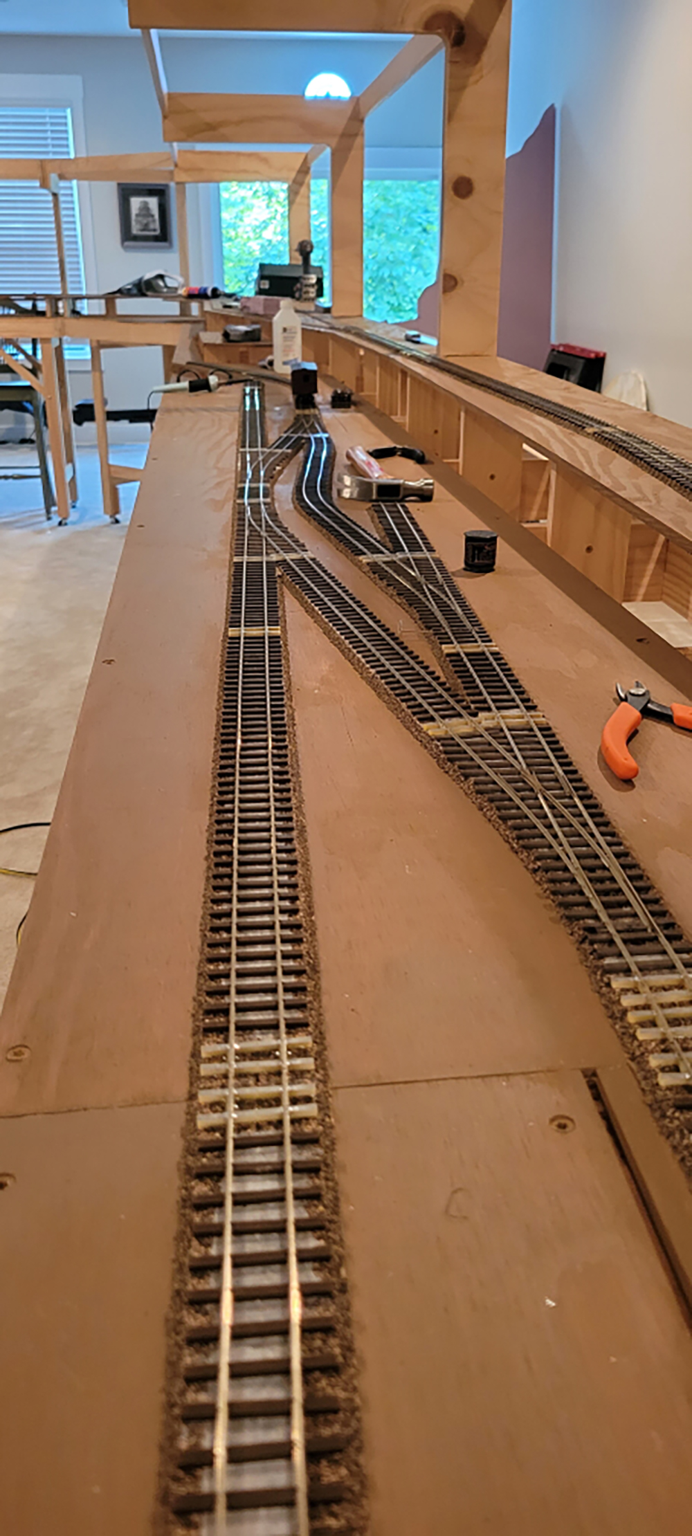 brown and sliver toy train track in straight and curved lines on a tan wood surface