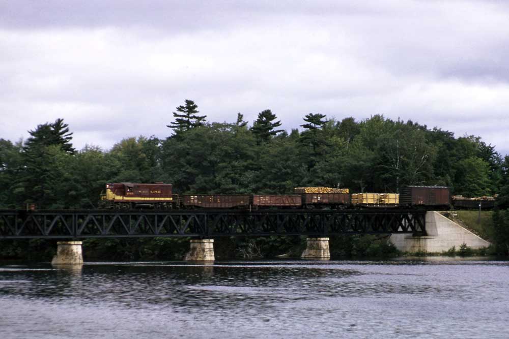 Maroon-and-gold diesel locomotive with freight train on bridge
