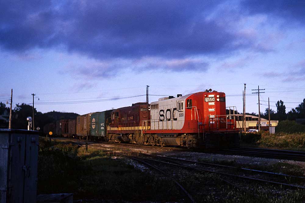 Red-and-white and maroon-and-gold Soo Line diesel locomotives on passenger train at sunset