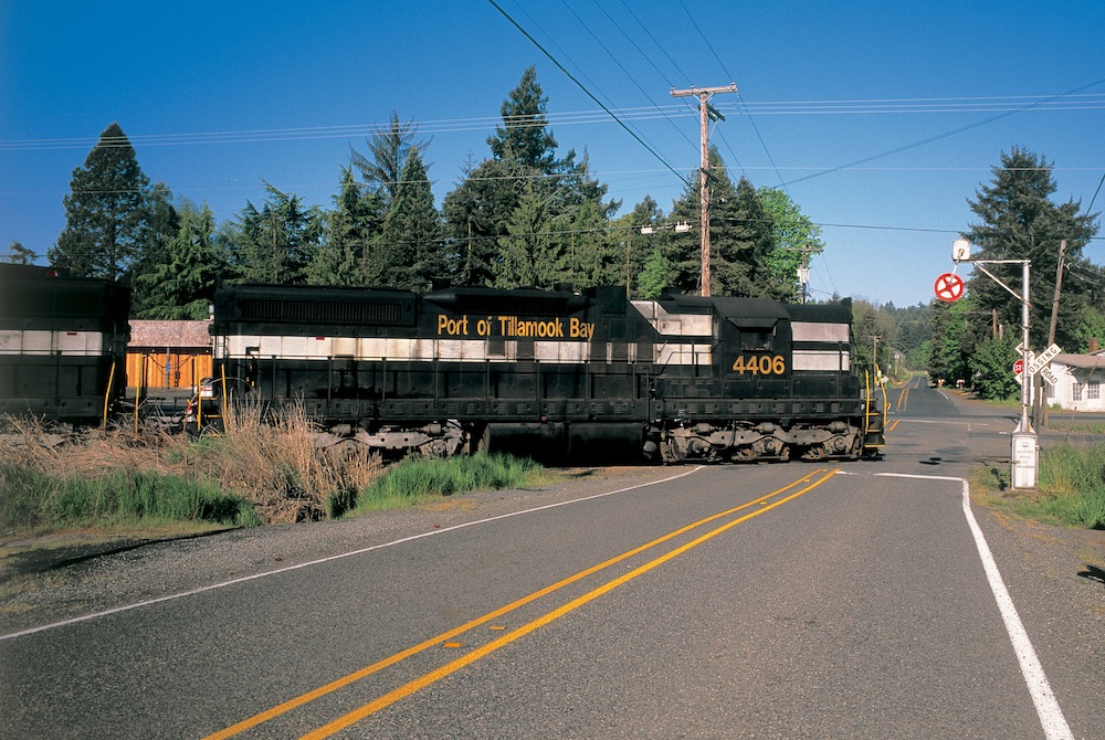 An image of a large, black and white freight diesel locomotive at a roadway crossing