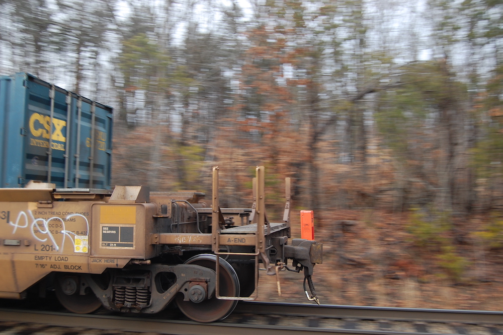 An orange end-of-train device is seen atop the rear coupler of a passing train. End-of-train devices replaced cabooses