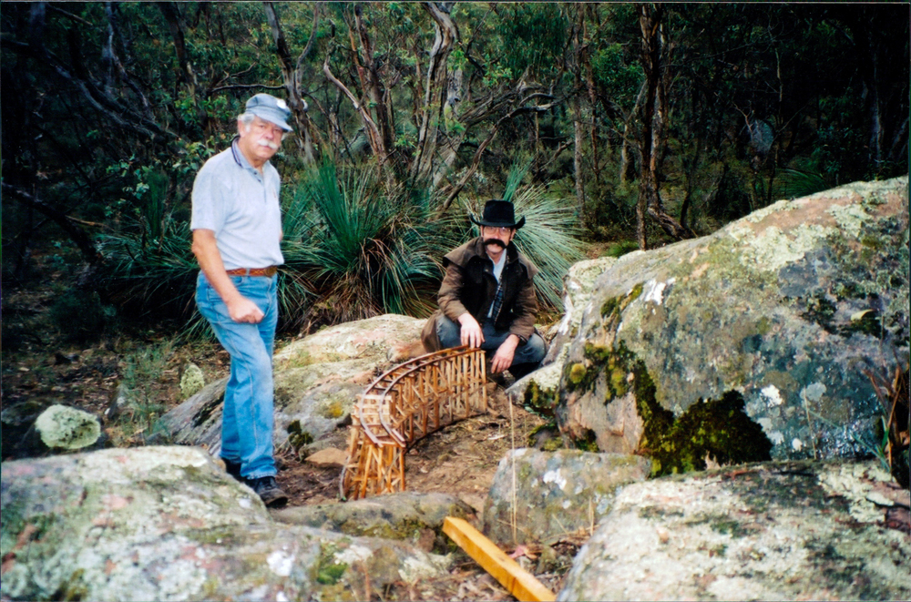 two men next to a model trestle and large rocks