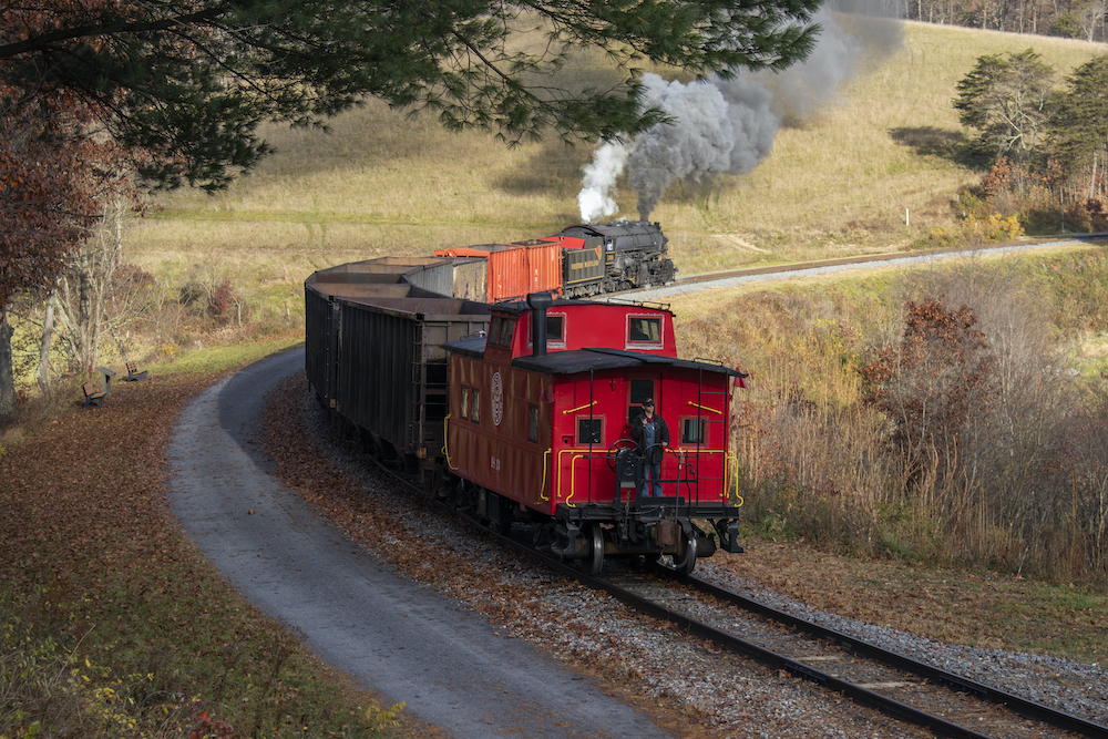 A red caboose trails a short freight train powered by a steam locomotive