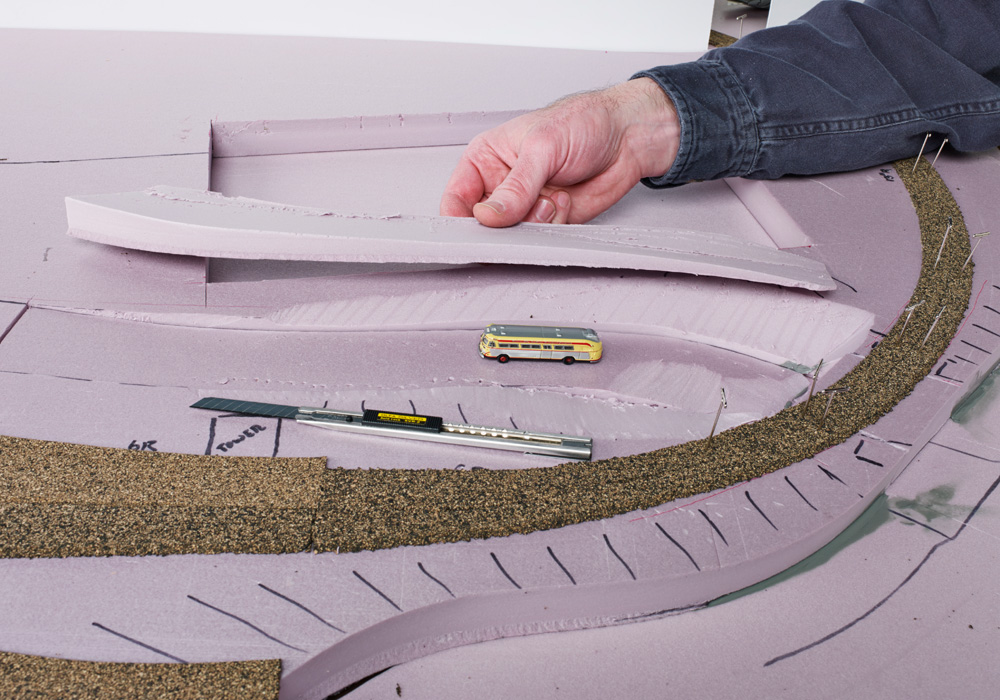 A hand reaches in to move a piece of pink foam board from an N scale layout under construction