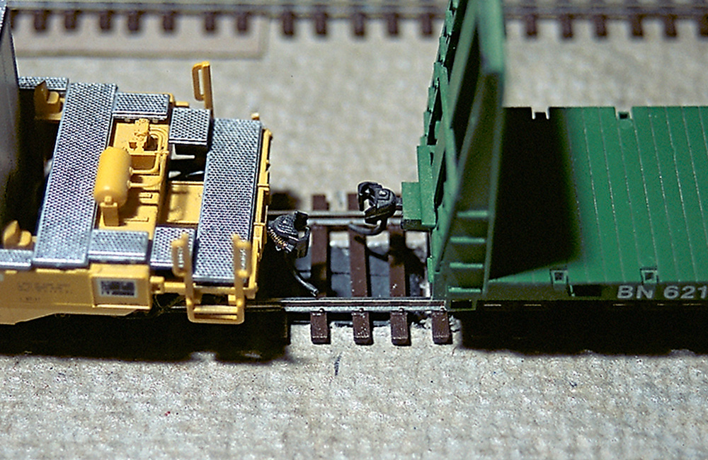 Two rail cars move toward each other with their couplers pulled apart by an under-track magnet