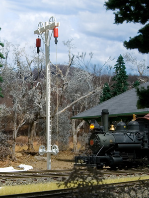 A small black steam locomotive passes a white trackside mast holding two red markers aloft on pulleys