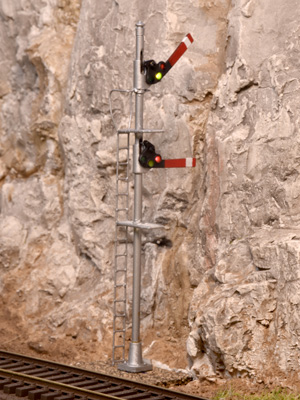 A two-bladed semaphore stands along a track in front of a rock wall