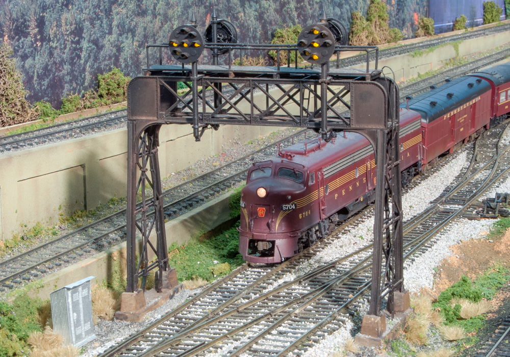 A dark red streamlined diesel leads a train under a signal bridge