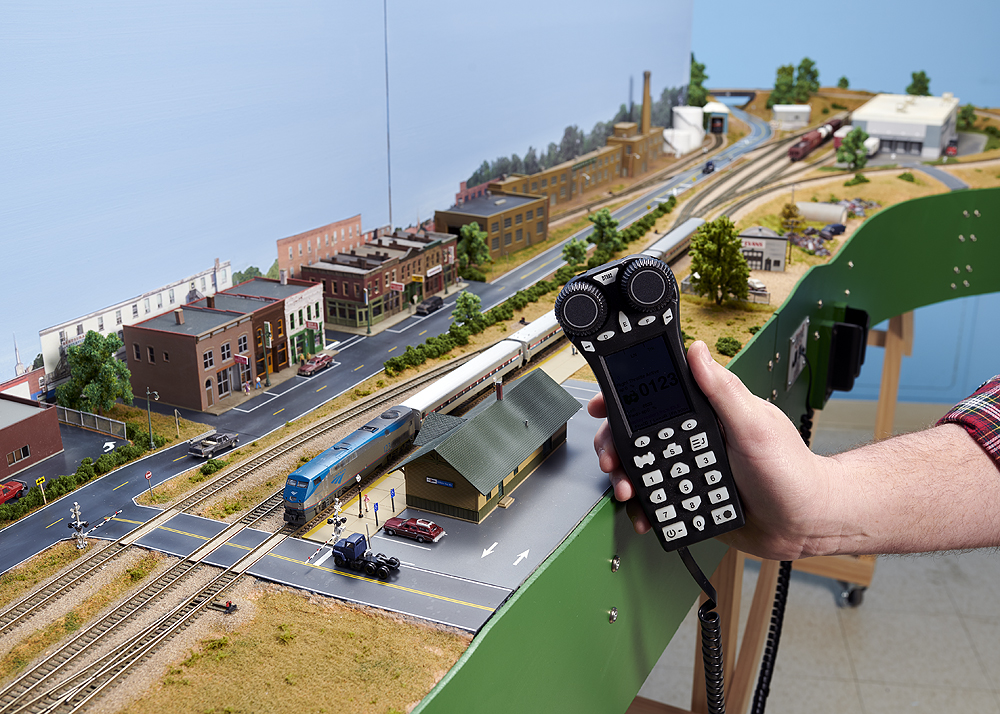 A new Digitrax throttle is held in front of an N scale train layout