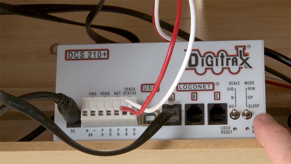A Digitrax command station sits on a wood shelf with wires coming from its front panel.