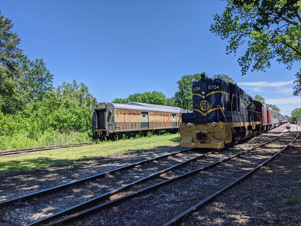 A diesel locomotive sits on a siding with passenger train behind it