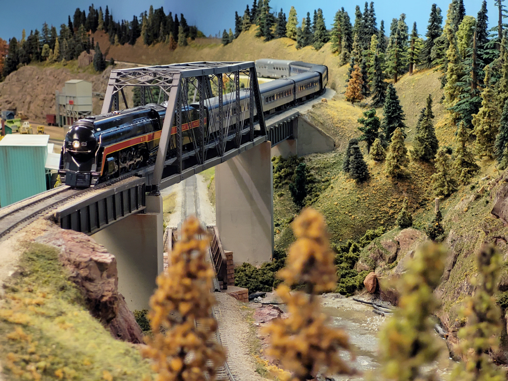 A model steam locomotive pulls a passenger train over a bridge